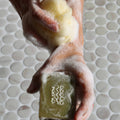 Hand holding a bar of soap with a brand logo against a tiled bathroom background