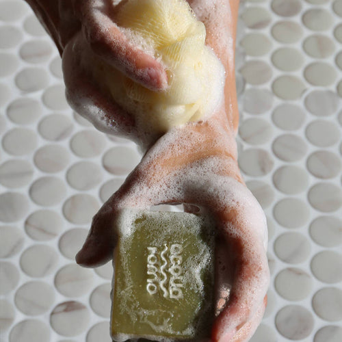 Hand holding a bar of soap with a brand logo against a tiled bathroom background