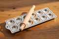 Metallic cookie stamp tray with a wooden rolling pin on a wooden surface